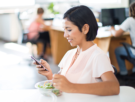 Woman smiling and eating a salad and looking at her phone