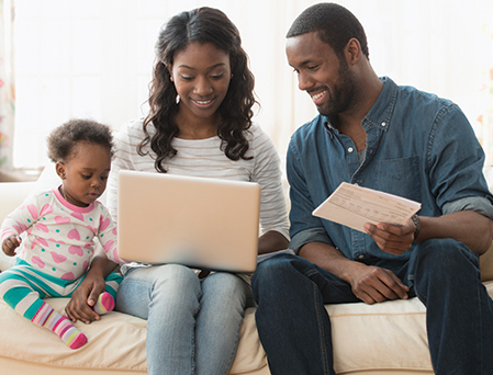30's African American man and woman with young child looking at a computer on sofa