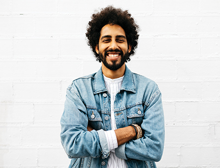 Mixed Race man with jean jacket and arms folded smiling